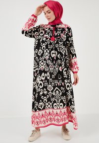 Long black dress with white and pink abstract patterns, featuring a wide collar, tassel detail, and elastic cuffs. Paired with light shoes.