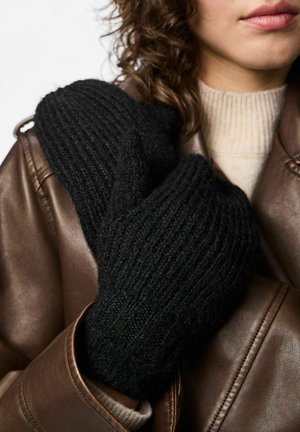 Moufles noires en tricot avec une texture côtelée. Les moufles sont portées sur une veste en cuir marron, rehaussées par un pull de couleur claire en dessous.