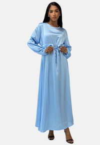 Abito maxi in satin azzurro chiaro con maniche lunghe, scollo rotondo e vita con cordino. Il tessuto ha una texture liscia con un design fluido.
