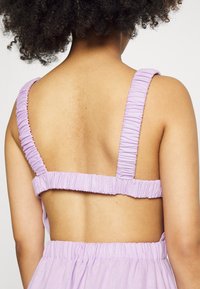 Vestido lilás com alças de tecido franzido, design de costas abertas e uma silhueta fluida. A textura parece suave e ligeiramente texturizada.