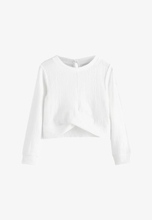 Biały długi rękaw crop top z teksturowanej tkaniny, z okrągłym dekoltem i węzłem z przodu. Posiada zapięcie na guziki z tyłu.