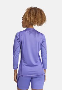 Paarse sportieve top met lange mouwen, een gladde textuur en een strakke pasvorm, met contrasterende naden en een sportieve silhouette.