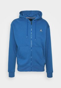 Sudadera azul con cremallera hecha de tela suave. Cuenta con un bolsillo canguro y cordones en contraste. Muestra un pequeño logo blanco de Jordan en el pecho.