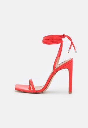 Rød høje hæle sandal med ankelrem og åben tå, med en slank stilet hæl og skinnende finish.