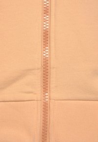 Felpa con zip color pesca chiaro, caratterizzata da un tessuto morbido, orlo a coste e una zip centrale con un tassello di plastica testurizzato.