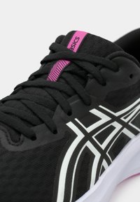 Μαύρο αθλητικό παπούτσι με λευκές λεπτομέρειες και υφή στην πάνω πλευρά. Διαθέτει ροζ λογότυπο στη γλώσσα και αντίθετους κορδόνες. Ελαφρύ σχέδιο.