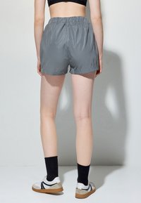 Grå, letvægts shorts med elastisk talje. Glat tekstur, længde til midten af låret, parret med sorte ankelstrømper og hvide sko.