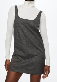 Robe à carreaux noir et blanc avec un décolleté carré, un design ajusté et des poches latérales, superposée sur un haut à col roulé blanc.