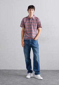 Κόκκινο και μπλε ριγέ πόλο μπλούζα με γιακά, συνδυασμένη με μπλε τζιν παντελόνι και λευκά αθλητικά παπούτσια. Απλή, casual εμφάνιση.