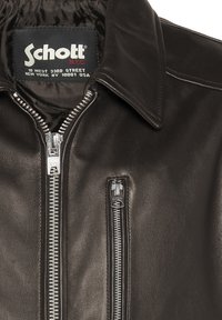 Chaqueta de motocicleta de cuero negro con cremallera frontal y cuello, con herrajes plateados y un pequeño bolsillo con cremallera. Etiqueta Schott en el interior.