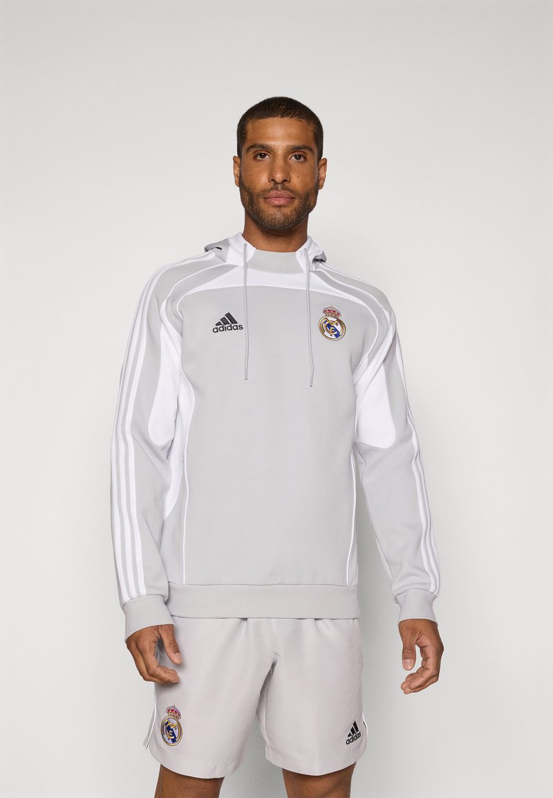 Siva Adidas dukserica s bijelim detaljima, logotip Real Madrida i kapuljača s vezicom. Par svijetlosivih kratkih hlača s logotipom.
