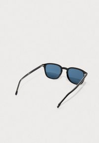 Μαύρα γυαλιά ηλίου με σκούρους μπλε φακούς, διαθέτοντας τετράγωνο σκελετό και λεπτά, κομψά μαύρα χερούλια. Μινιμαλιστικός σχεδιασμός χωρίς ορατά σχέδια.