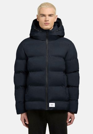Navy pufferjack met een capuchon, voorzien van een rits aan de voorkant en twee zijzakken. Zachte, gestepte textuur met een merklabel aan de zoom.