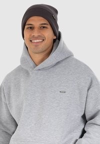 Felpa grigia con un grande cappuccio e una piccola etichetta con logo. Abbinata a un berretto a coste grigio scuro, con un motivo a maglia testurizzata.