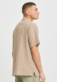 Short-sleeve checkered shirt in beige and brown tones, featuring a relaxed fit, side slits, and a classic collar.
