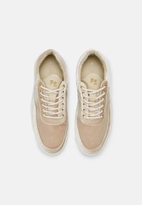 Paire de baskets en daim beige avec des lacets crème et des œillets dorés, vues de dessus sur un fond gris clair.