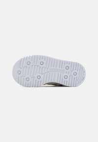 Semelle de chaussure avec un design texturé et strié, des poignées circulaires, de couleur principalement blanche, et un logo de marque visible au centre.