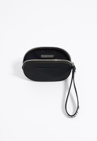 Funda negra con cremallera de exterior de tela, que cuenta con una correa para la muñeca y un logotipo en relieve. Forma ovalada compacta con una cremallera plateada.
