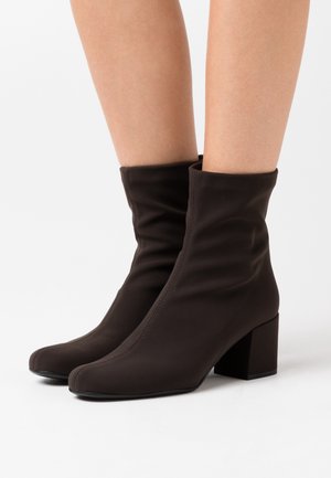 Brown ankle boots made of a soft, stretchy material with a square toe and a chunky block heel. Wrinkled design at the ankle for detail.