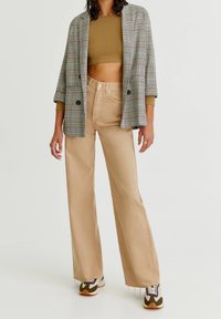 Beżowe spodnie z szerokimi nogawkami połączone z krótki oliwkowym topem z prążkowanego materiału oraz dużą marynarką w kratę, z brązowymi, białymi i zielonymi akcentami.