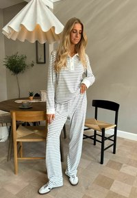 Svijetlosivi i bijeli prugasti loungewear sadrži majicu s ovratnikom i dugim rukavima te hlače širokog kroja, uparen s bijelim tenisicama.