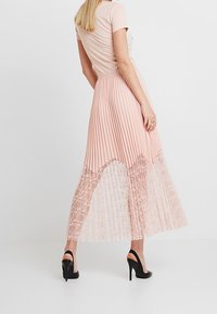 Robe rose clair avec un haut ajusté et une jupe plissée, présentant un ourlet en dentelle. Les manches sont courtes et le tissu a une texture douce.