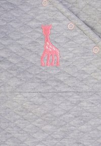 Tessuto grigio trapuntato con una giraffa ricamata in rosa. Presenta motivi a rombi e bottoni a pressione rosa lungo il bordo.