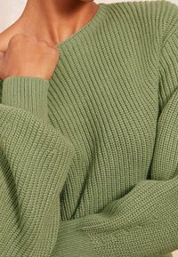 Pull vert en tricot avec une texture côtelée, doté d'un large col et de manches longues. Le matériau semble doux et chaud.