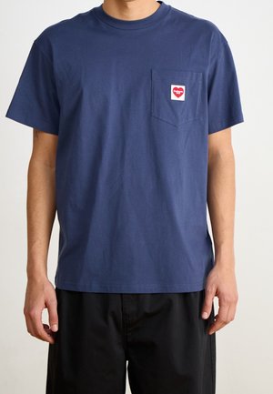 T-shirt en coton bleu marine avec une poche poitrine ornée d'un logo en forme de cœur. Manches courtes et col rond classique complètent le style.