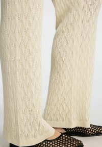 Cremefarvede strikkede bukser med et bølge mønster, tekstureret finish og ribbet kant. Matchet med sorte mesh slip-on sko.