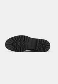 Black rubber shoe sole with treads for traction, featuring a central zigzag pattern and branding. Flat profile, durable design for outdoor use.