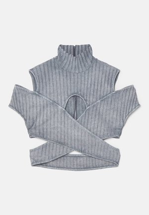 Top croisé gris à côtes avec découpes aux épaules. Pantalons noirs taille haute avec un motif abstrait brillant et des jambes évasées, assortis à des talons pointus.