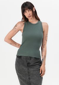 Grønn ribbet tanktop med høy hals og ermeløs design, kombinert med et svart denimskjørt med rett snitt.
