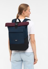 Táska, amely hengertetejű kialakítású, sötétkék és bordó színben, elülső zsebbel és állítható pántokkal. Tartós anyagból készült.