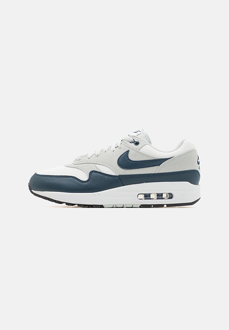 Nike Air Max 1 -kengät valkoisena ja tummansinisenä, joissa on nahka- ja verkkomateriaali, pyöreä kärki, pehmustettu kaulus ja näkyvä ilmatyyny.