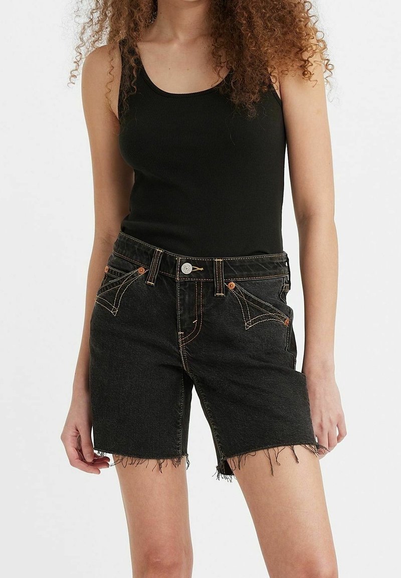 Shorts en denim noir avec ourlet effiloché, cinq poches et surpiqûres orange contrastantes. Associés à un débardeur noir côtelé ajusté.