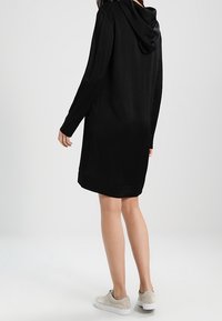 Abito nero con cappuccio, maniche lunghe, vestibilità casual e tasche laterali. Tessuto morbido e design fino al ginocchio. Abbinato a sneakers chiare.