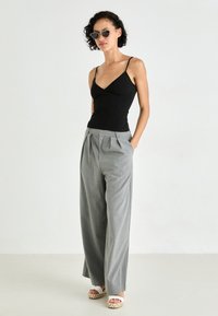Top noir à fines bretelles, associé à un pantalon large à rayures grises. Le mannequin porte des lunettes de soleil rondes et des sandales à plateforme.