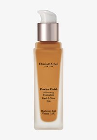 Fond de teint Flawless Finish dans un flacon en verre transparent. Distributeur à pompe, liquide beige, texte noir, capuchon argenté, mentionne de l'acide hyaluronique et des vitamines C et E.
