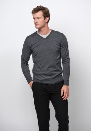 Grijze v-hals trui, gebreide stof, lange mouwen, geribbelde manchetten en zoom, over een lichtgrijze t-shirt gelaagd. In combinatie met zwarte broeken.
