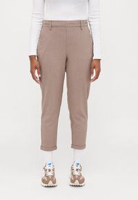 Ljust bruna skräddarsydda byxor med en slät yta, smal passform och uppvikta benslut, som bärs tillsammans med vita strumpor och beigefärgade sneakers.