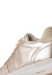 Metallic gold sneaker with perforated design, textured heel accent, and white sole. Features soft material and stitched detailing.