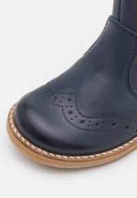 Námořnické kožené kotníkové boty s kulatou špičkou, brogue detaily a kontrastní světle hnědou podrážkou se šitým okrajem.