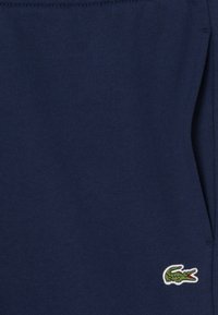 Temno modre bombažne trenirke z rebrastim pasom, na levi strani je izvezen majhen zeleni krokodil.