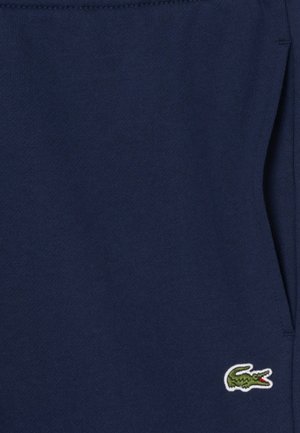 Temno modre bombažne trenirke z rebrastim pasom, na levi strani je izvezen majhen zeleni krokodil.