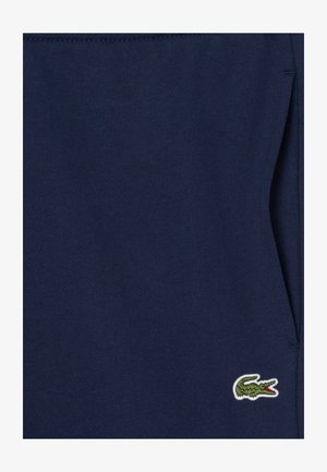 Tmavomodré bavlnené tepláky s rebrovaným pásom, na ľavej strane zdobené malým zeleným vyšitým logom krokodíla.