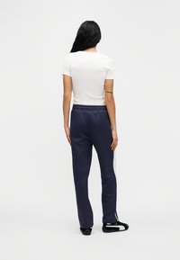 Άσπρο κοντομάνικο μπλουζάκι σε συνδυασμό με σκούρο μπλε παντελόνι φόρμας με λευκή ρίγα στο πλάι και ελαστική μέση, εμφανιζόμενο από πίσω.