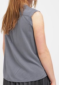 Ärmlös topp i ett svartvitt geometriskt tryck, med krage och slätt texturerat tyg.