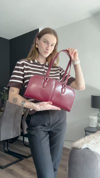 Burgundy leather handbag with a structured design, dual handles, and oval hardware accents. Smooth texture with a shiny finish.