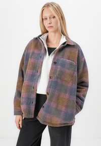 Giacca in pile a quadri con un motivo plaid multicolore in viola, blu e marrone, con chiusura a bottoni e tasca sul petto.